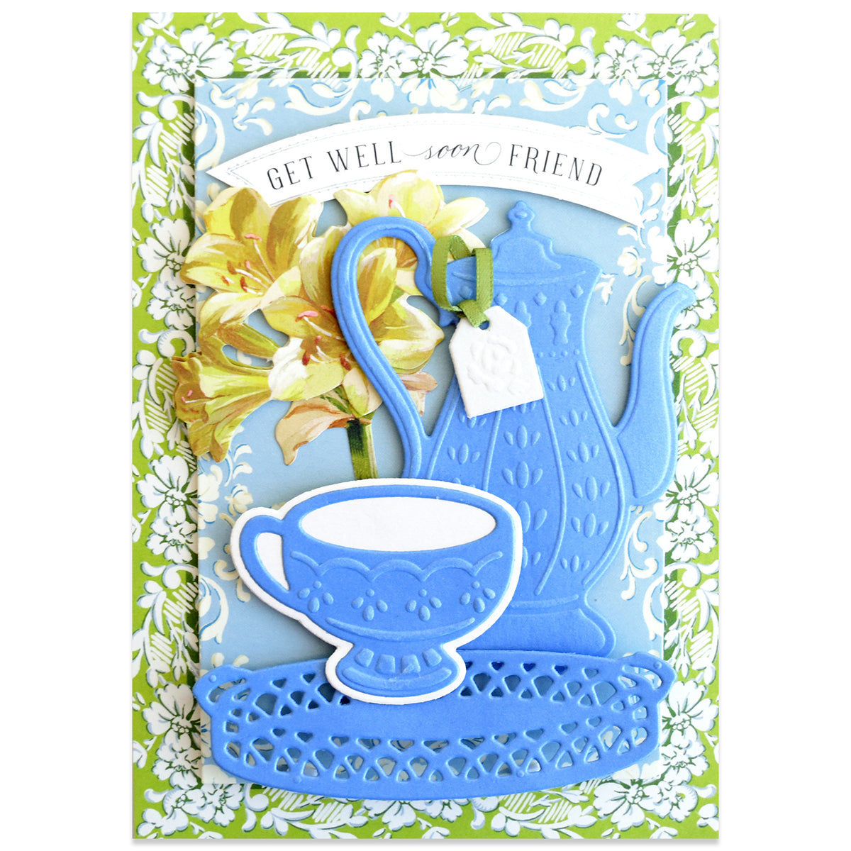 Greeting card with “Get well soon friend” text, featuring a blue teapot, teacup, a floral background, and a tea bag tag hanging near yellow flowers. Beautiful tea-inspired embellishments and intricate details created using the Tea Party Cut and Emboss Dies by Anna Griffin add elegance to this charming design.