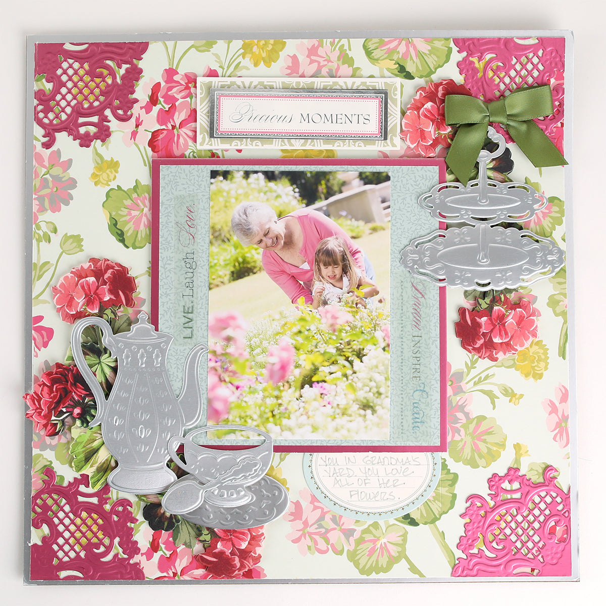 Scrapbook page featuring a photo of an older woman and child in a garden, accented with floral patterns and tea-inspired embellishments such as silver teapot, cup, and cake stand details crafted using the Tea Party Cut and Emboss Dies by Anna Griffin.