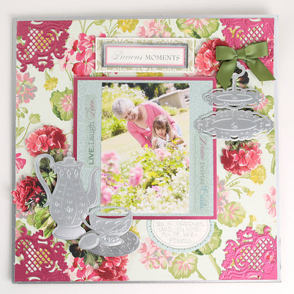 Scrapbook page featuring a photo of an older woman and child in a garden, accented with floral patterns and tea-inspired embellishments such as silver teapot, cup, and cake stand details crafted using the Tea Party Cut and Emboss Dies by Anna Griffin.