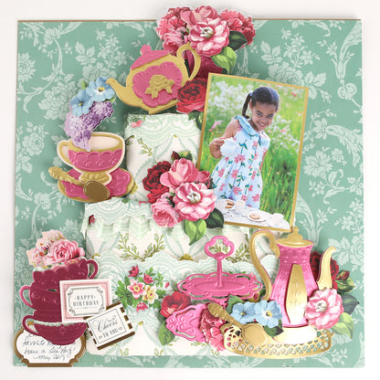 A scrapbook page with floral decor, teapots, teacups, and a photo of a young girl at a tea party, all arranged on a green patterned background and beautifully accented with Tea Party Cut and Emboss Dies for charming craft embellishments.