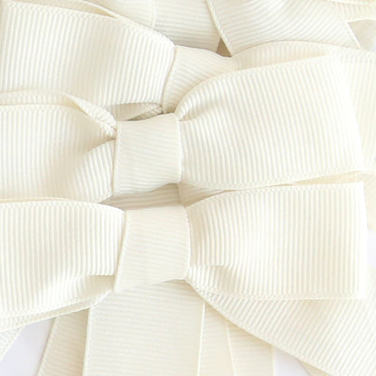 Several Pre-Tied Bows with Tails in white and platinum grosgrain ribbon are closely arranged, highlighting their textured fabric and neatly tied loops.