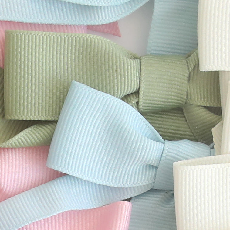A close-up of several Pre-Tied Bows with Tails in ribbed pastel fabrics—pink, green, blue, and platinum off-white—layered delicately together.