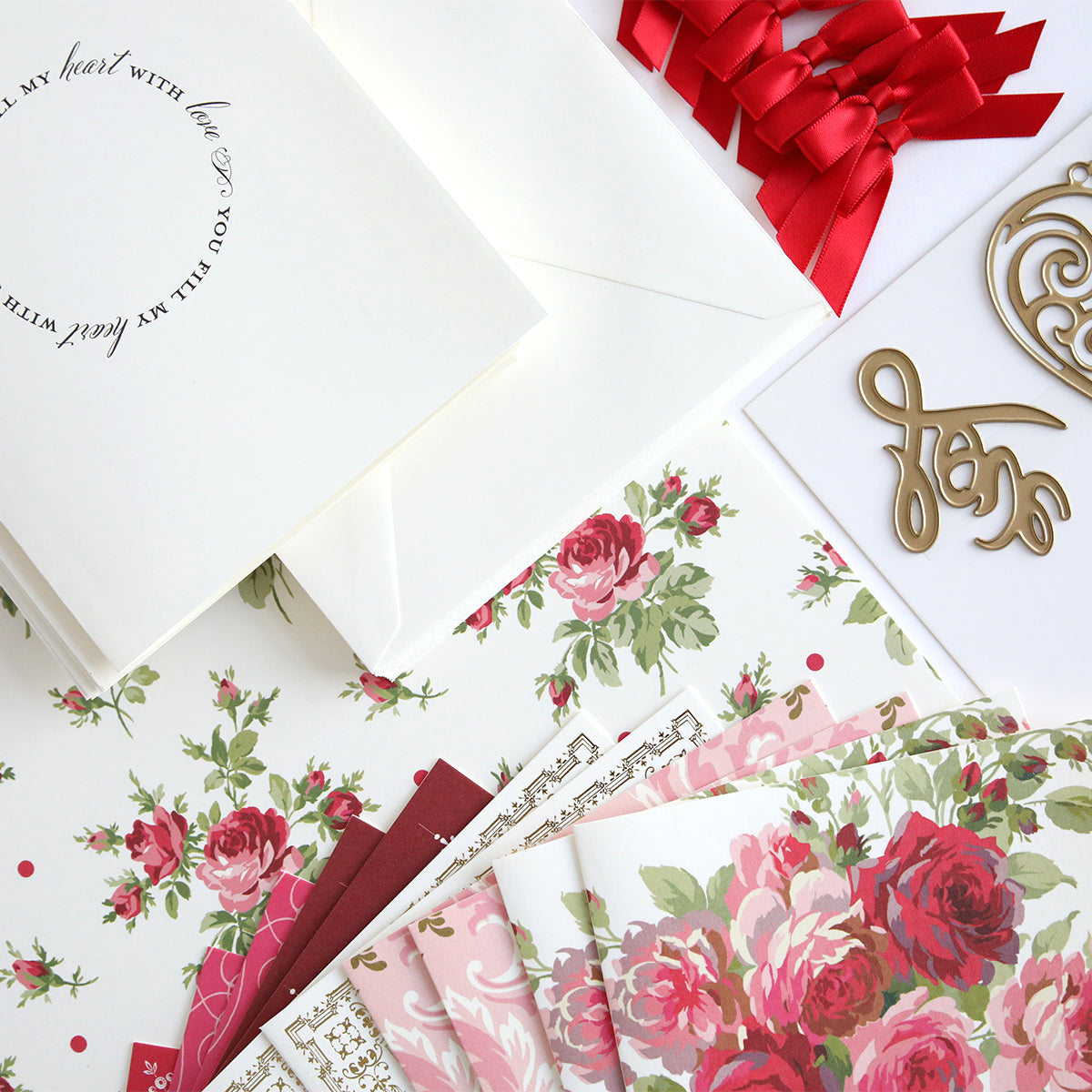 Floral-patterned papers, white envelopes, a card with cursive text, red ribbon, and metallic accents—ideal for elevating your crafts or discovering the Anna Griffin® 2026 Papercrafting Mystery Box Subscription.
