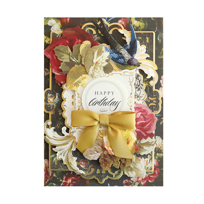A birthday card featuring the Anniversary Paper Crafting Collection, adorned with a gold ribbon and floral designs.