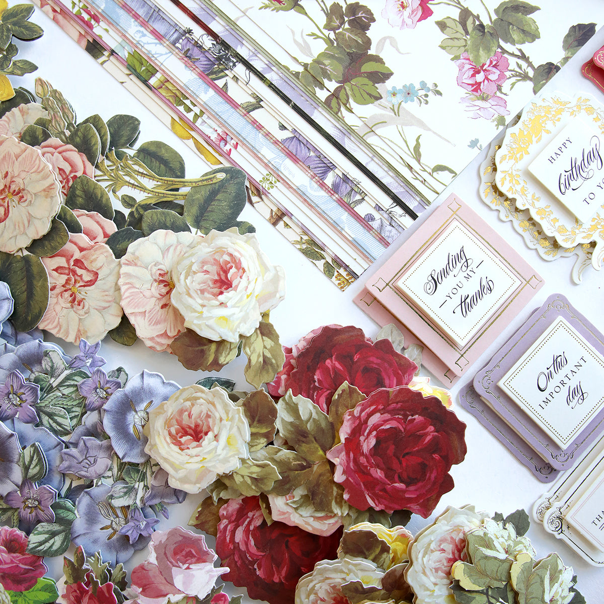 Anniversary Paper Crafting Collection's first designs of floral paper flowers and cards are laid out on a table for scrapbooking.