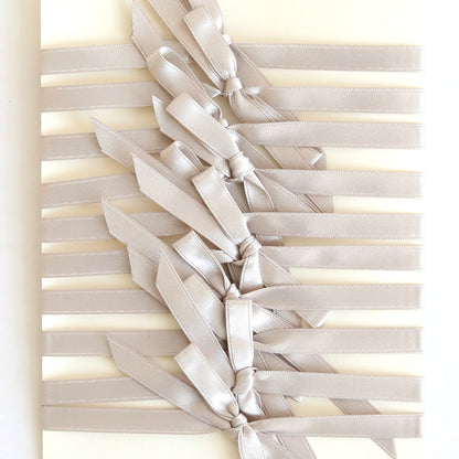 A cream background with multiple parallel pre-tied Silver Satin Bows (10 count), each neatly tied down the center—perfect for accenting handmade cards.