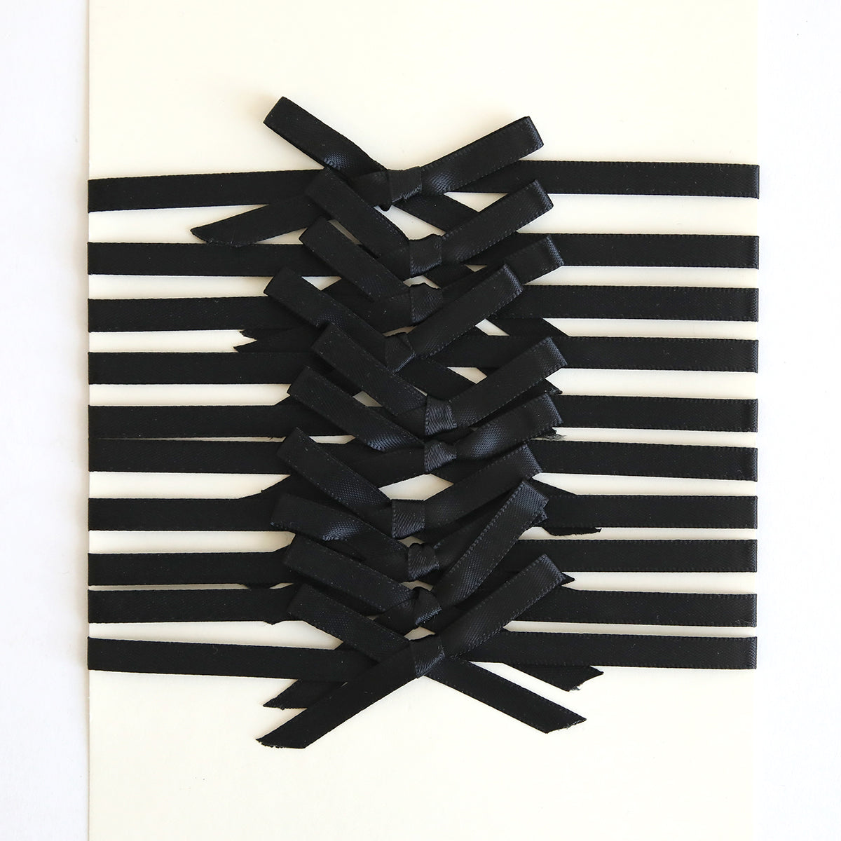 The Black Satin Bows 10 count features black ribbon embellishments arranged in a crisscross pattern on a white surface, forming elegant satin bows at the center.
