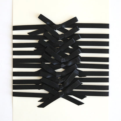 The Black Satin Bows 10 count features black ribbon embellishments arranged in a crisscross pattern on a white surface, forming elegant satin bows at the center.