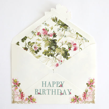 A handmade floral birthday card partially inserted into an envelope with "Happy Birthday" written on the front. Both the card and envelope are adorned with intricate floral designs, complemented by elegant foil accents from the Birthday Greetings Envelope Liners collection.