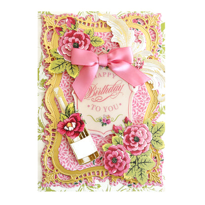 Handcrafted birthday card with floral design and 3D elements, featuring a pink bow, champagne bottle, and Happy Birthday rub-on transfers.