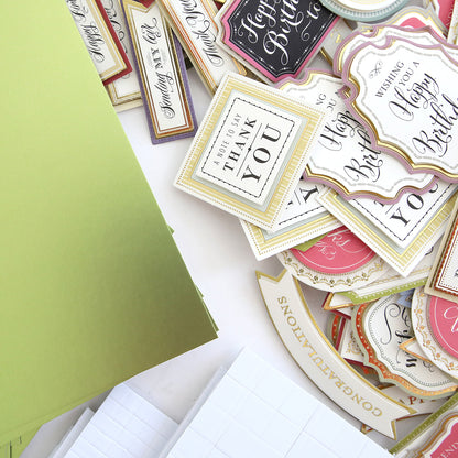 The Create Supply Box includes green envelopes and assorted decorative greeting card tags with celebratory messages, featuring 3D Sentiment Stickers and Matte Foil Cardstock for crafting elegant event supplies.