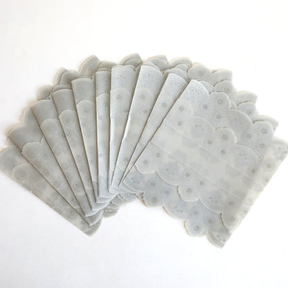 Ten silver vellum gatefold wraps with scalloped edges are fanned out on a white surface, ideal for elegantly presenting invitations. Available as a 10 pack.