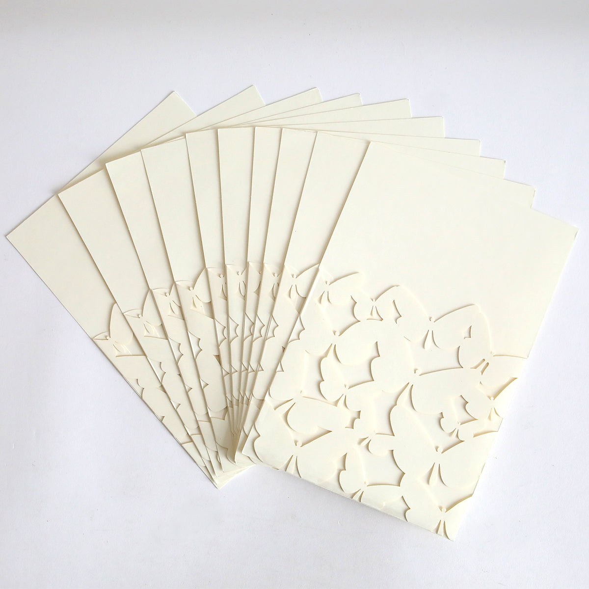A pack of ten Ivory Butterfly Diecut Pocket cards features cream-colored, embossed floral cut-out designs and elegant ivory butterfly pockets, displayed fanned out on a flat white surface.