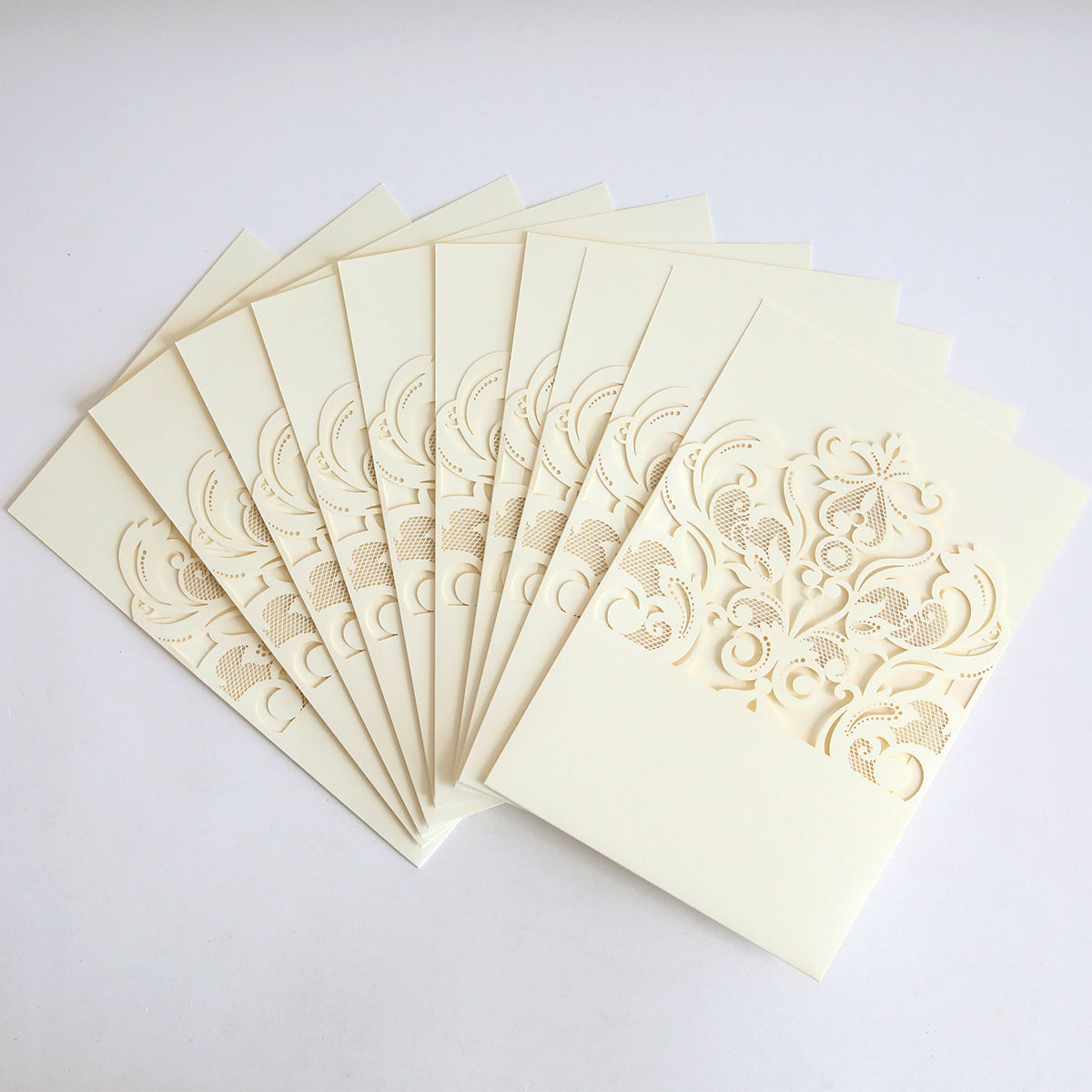 The Ivory Laser Cut Pocket 10 pack features ten cream-colored wedding invitations with ornate ivory lace laser-cut pockets, displayed in a fanned arrangement on a white background.