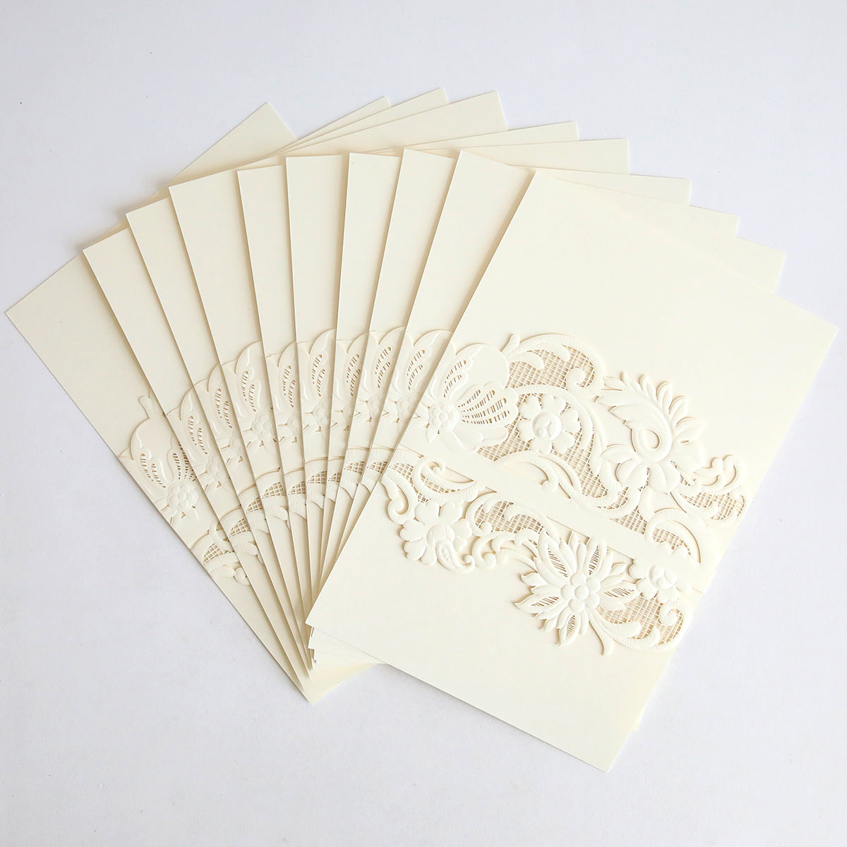 A stack of invitation cards wrapped in Ivory Laser Cut Lace Belly Band (10 pack) is displayed in a fan shape on a white background, showcasing the cream-colored embossed floral designs and elegant lace details.
