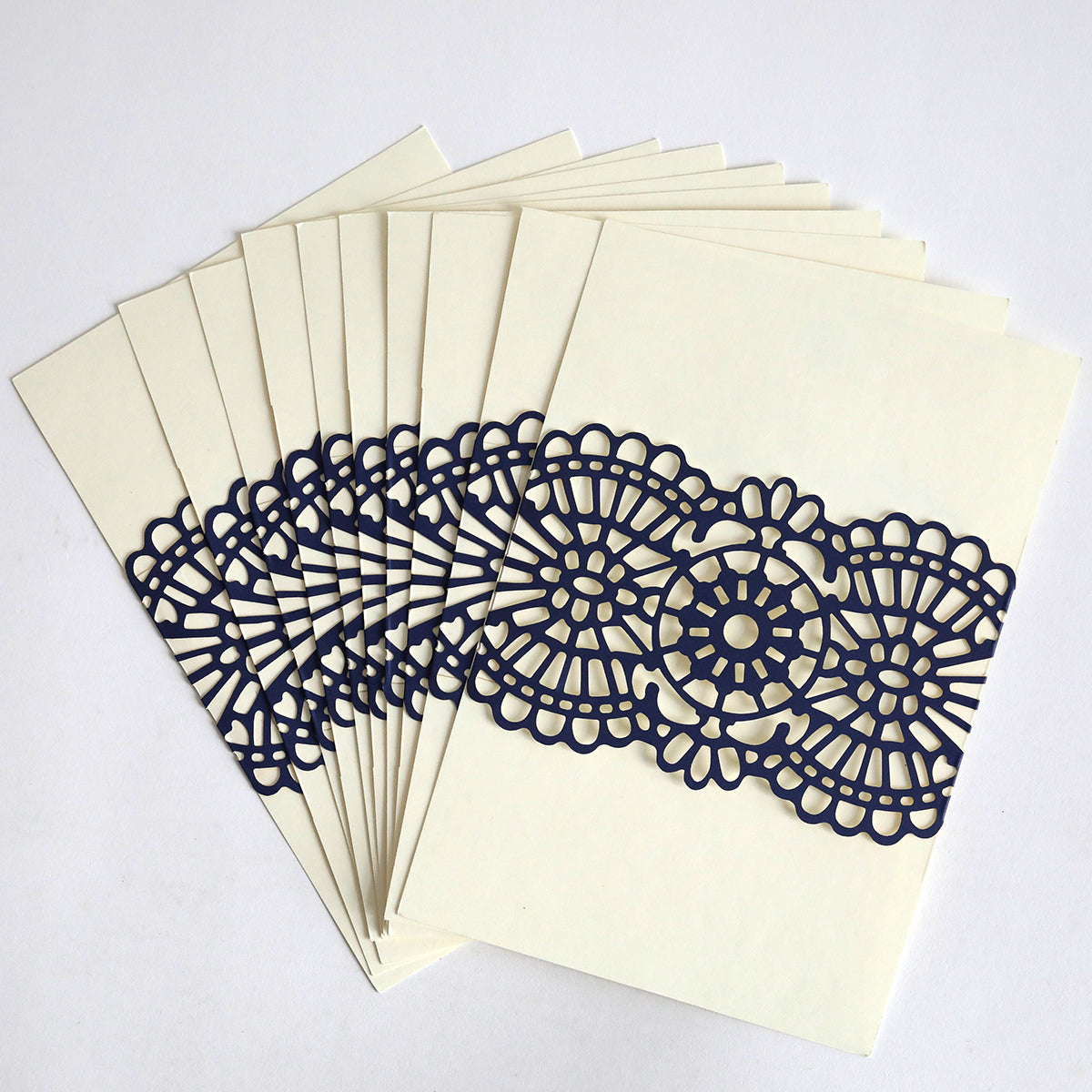 A set of cream-colored wedding invitations from the Navy Lace Band 10 pack is fanned out, each featuring an elegant navy blue, laser-cut lace design across the center.