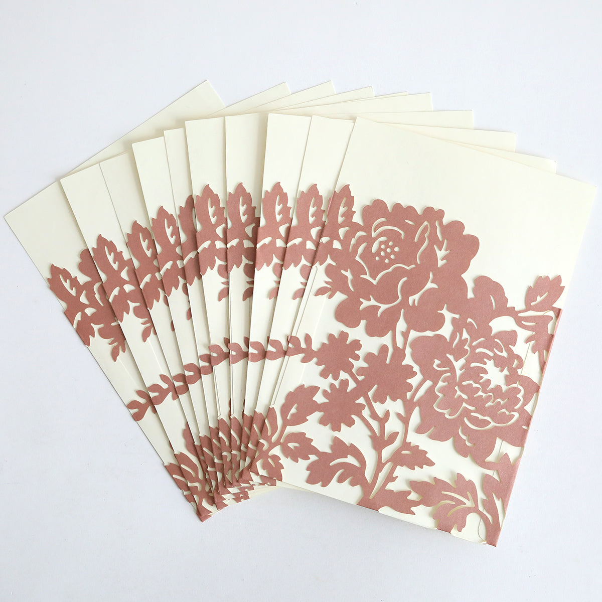 A fan arrangement of Rose Gold Rose Diecut Pocket invitations (10 pack), featuring cream cards with metallic pink floral designs, displayed on a white surface.