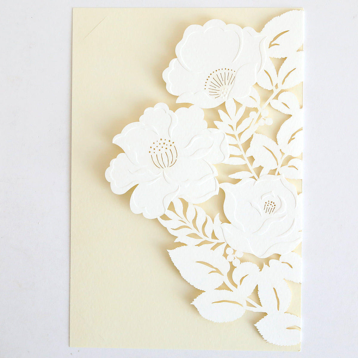 The Floral Diecut Invitation 10 pack features cream cards with three white, intricately cut-out flowers and leaves on the front, offering a delicate floral design—ideal for pairing with embossed floral invitation wraps.