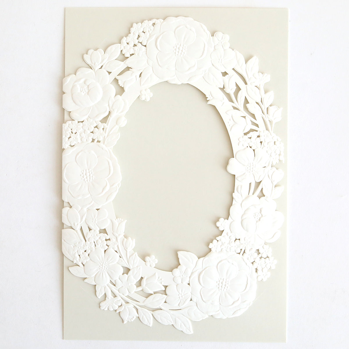 The Floral Wreath Laser Cut Invitation 10 pack features embossed white oval frames with delicate flower and leaf patterns on a pale background. The blank center is perfect for customizing your wedding invitation wraps.