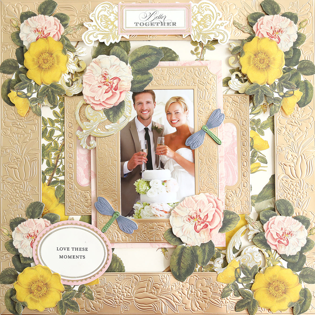 A framed photo of a couple celebrating, surrounded by ornate floral decorations and dragonfly cutouts made from Champagne Matte Foil Cardstock, with a sign reading "Love These Moments.