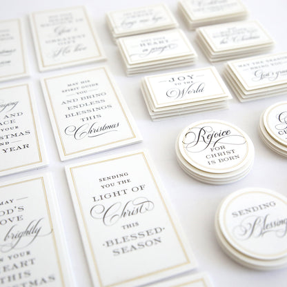 Christmas Blessings Sentiment Stickers feature assorted rectangular and circular white stickers with elegant black script, displaying Christmas and Christian-themed messages, all arranged neatly on a white surface.