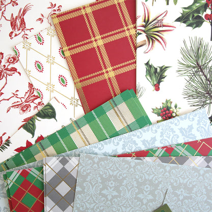 Various 12x12 sheets of festive wrapping paper from the Christmas Cardstock Collection featuring Christmas-themed designs such as plaid patterns, holly, pine branches, and floral prints are spread out.