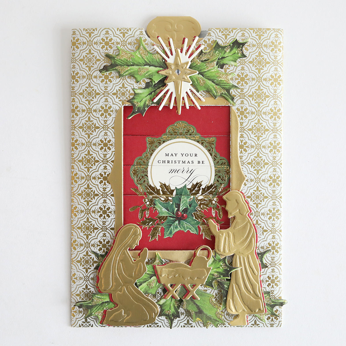 The Christmas Clever Sliding Scenes Cardstock is a decorative Christmas card with gold silhouettes of Mary, Joseph, and baby Jesus, holly accents, ornate patterns, and an interactive message: "May your Christmas be merry.