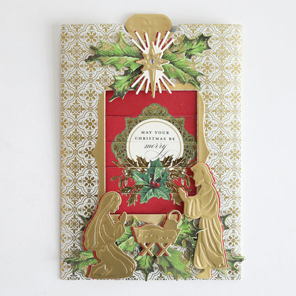 The Christmas Clever Sliding Scenes Cardstock is a decorative Christmas card with gold silhouettes of Mary, Joseph, and baby Jesus, holly accents, ornate patterns, and an interactive message: "May your Christmas be merry.