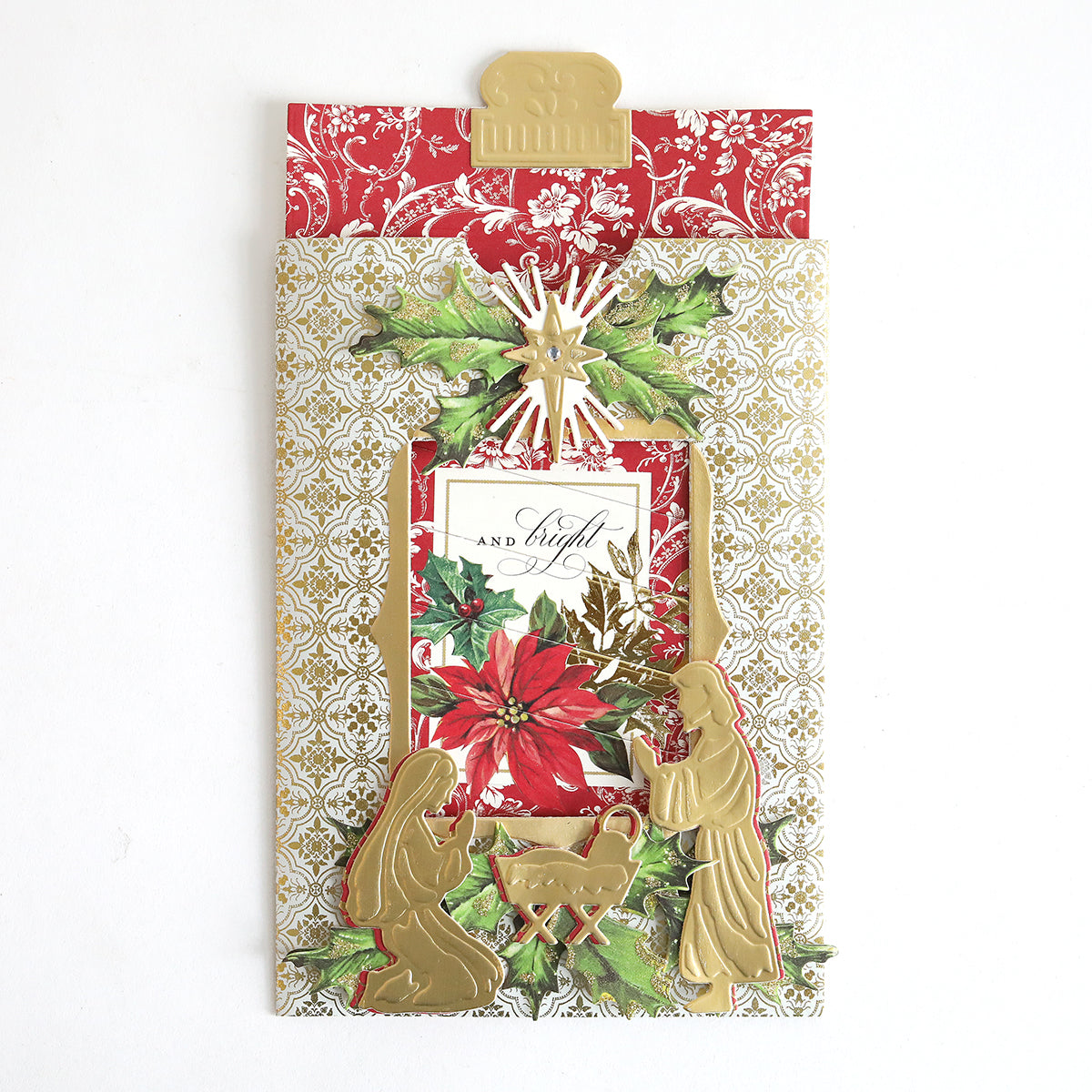 A decorative Christmas card made with Christmas Clever Sliding Scenes Cardstock, featuring a gold nativity scene, poinsettia flower, and ornate red and gold patterned background using sliding card dies.