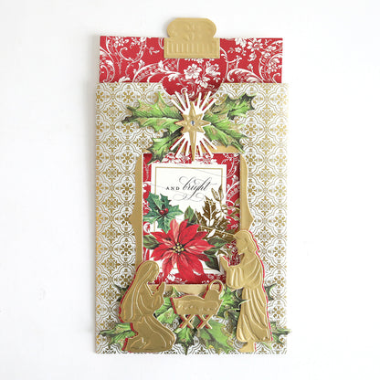 A decorative Christmas card made with Christmas Clever Sliding Scenes Cardstock, featuring a gold nativity scene, poinsettia flower, and ornate red and gold patterned background using sliding card dies.
