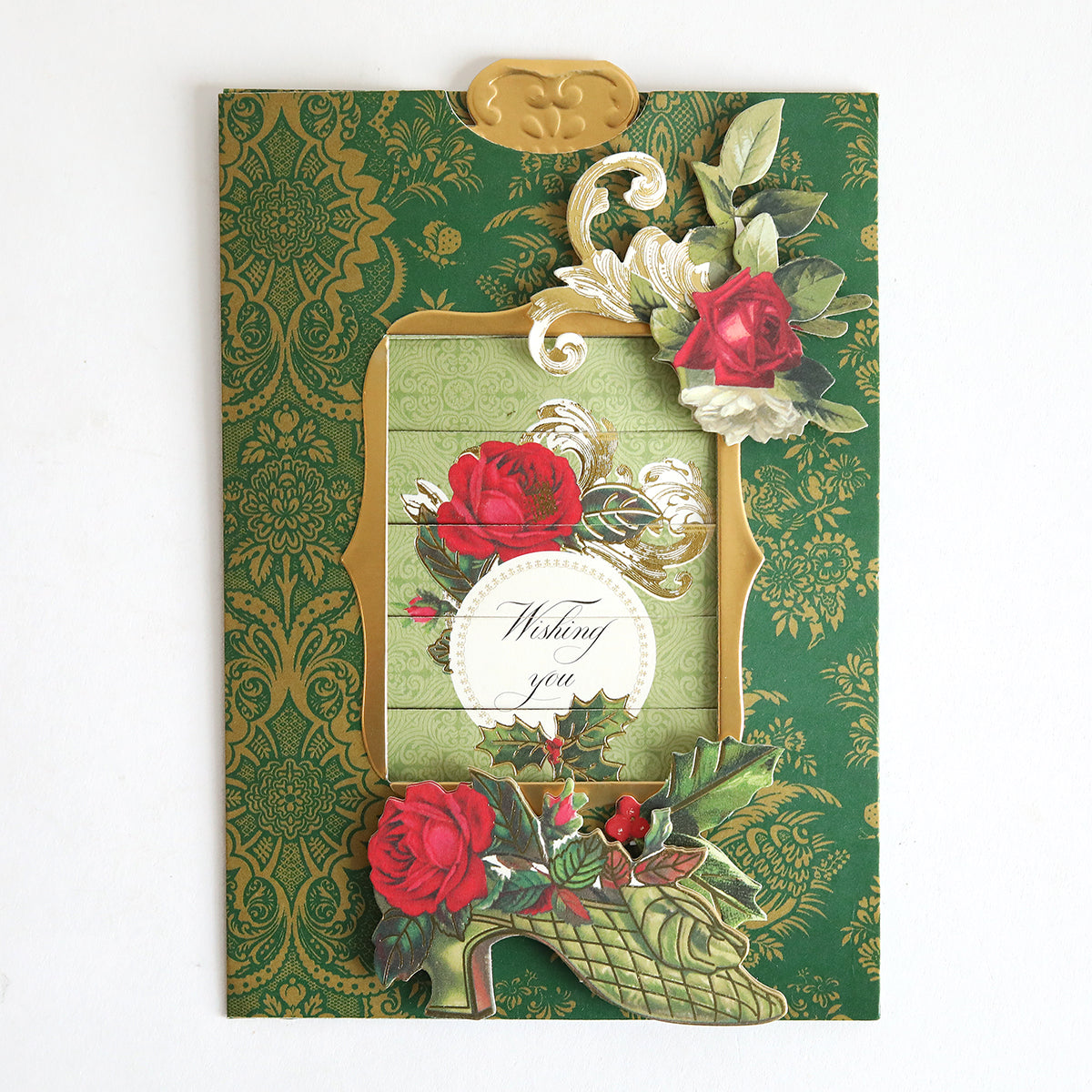 The Christmas Clever Sliding Scenes Cardstock is a decorative green greeting card with gold patterns, red roses, ornate floral designs, and an interactive sliding message reading "Wishing you" in the center.