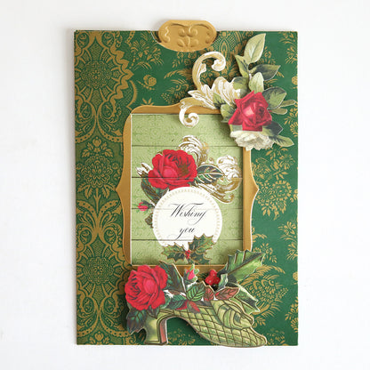 The Christmas Clever Sliding Scenes Cardstock is a decorative green greeting card with gold patterns, red roses, ornate floral designs, and an interactive sliding message reading "Wishing you" in the center.
