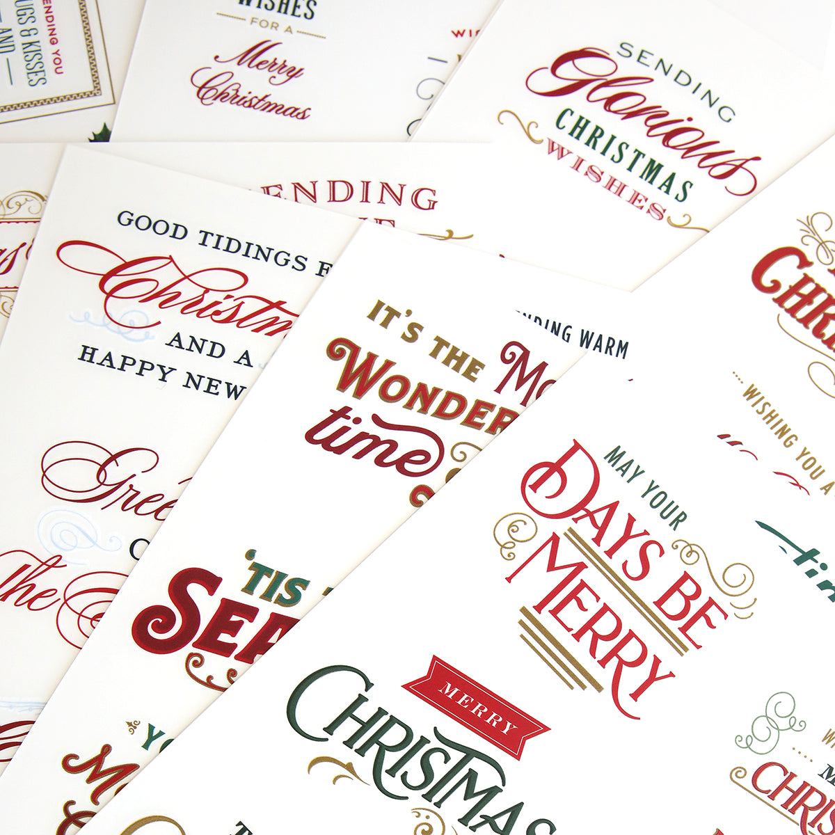 Various Christmas cards with festive messages and designs are spread out, featuring phrases like "Merry Christmas," "Good Tidings," and "May Your Days Be Merry." They include high quality Christmas Greetings Rub On Transfers for an elegant and enhanced touch.