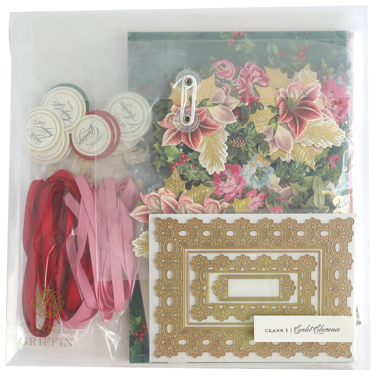 The Eyelet Elegance Dies and Materials kit includes floral paper, decorative frames, satin ribbons, seals, a metal clasp, and elegant embellishments, all neatly arranged in a clear plastic bag.