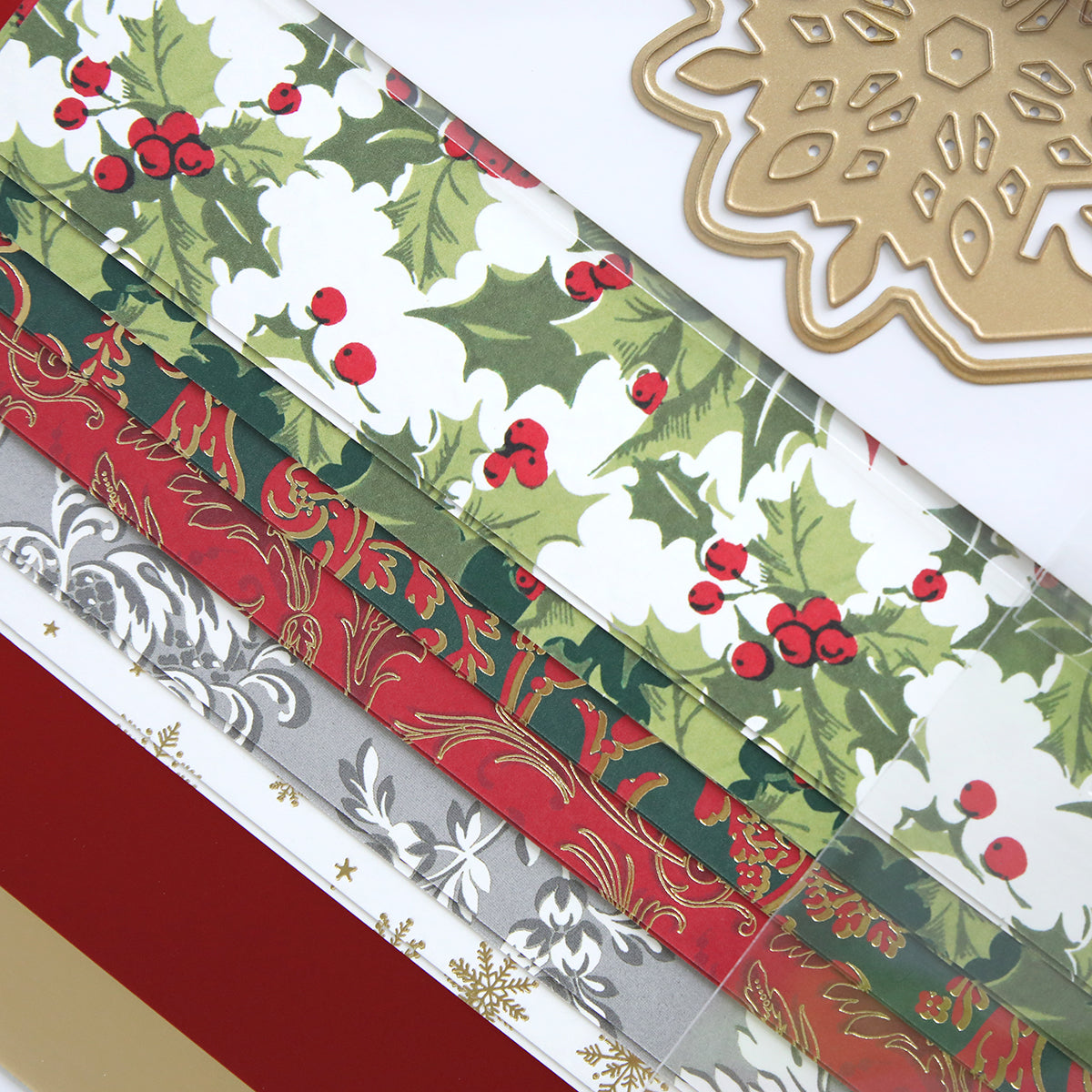The Festive Tags Dies and Materials showcase intricate holiday patterns with holly leaves and berries, adorned with gold and red designs intertwined with satin ribbons, complemented by a gold snowflake cutout set against a white backdrop.