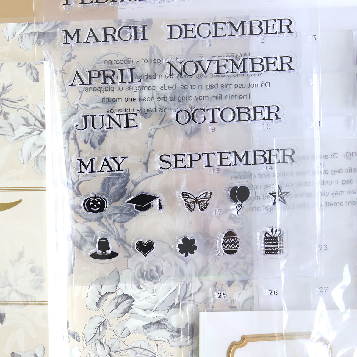 The Creative Calendar Stamps, Dies and Materials set features clear stamps with the months and icons such as a pumpkin, graduation cap, and butterfly on a floral backdrop. It's ideal for use with Creative Calendar Dies or cardstock projects and also includes symbols like a balloon, top hat, dollar sign, heart, snowflake, and gift box.