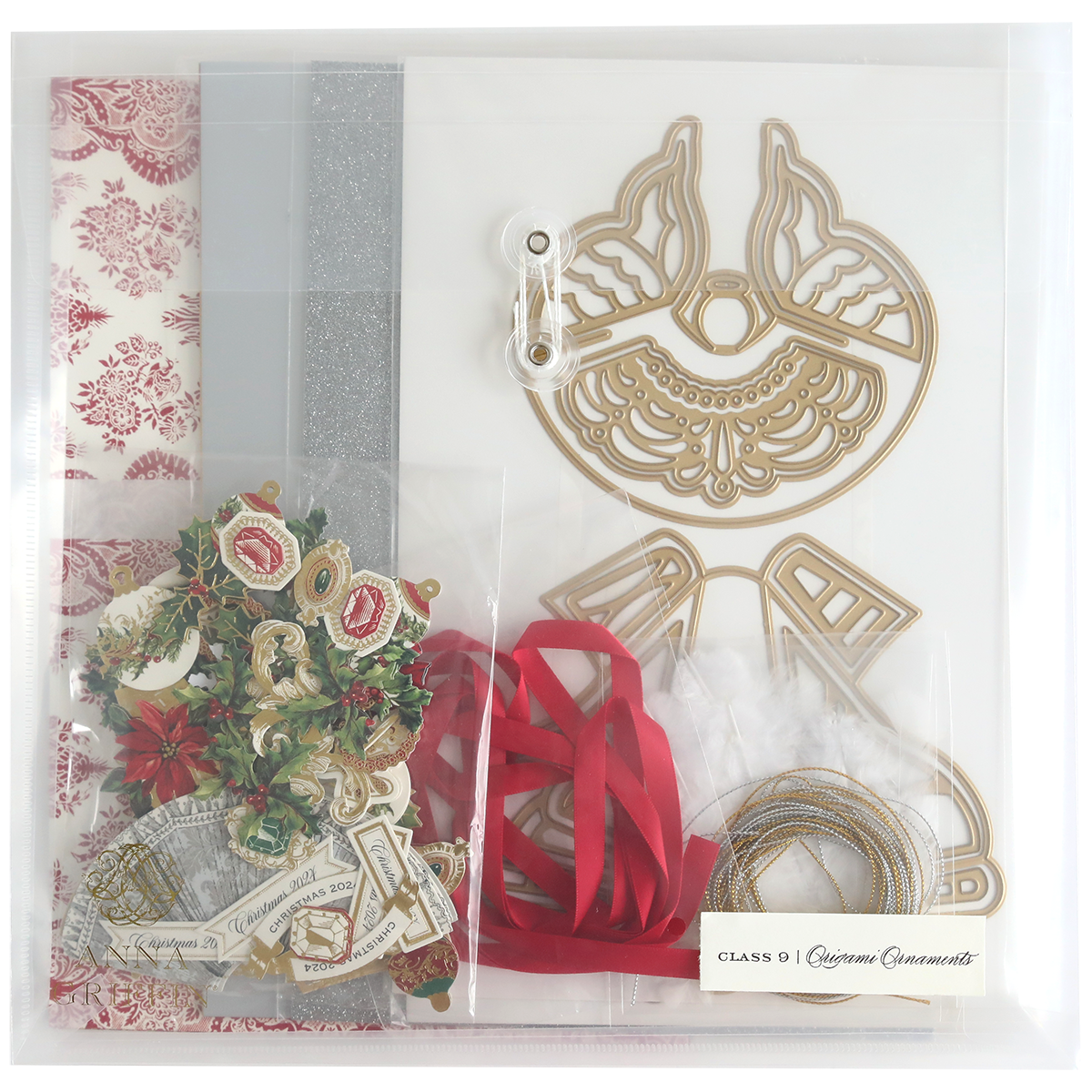 The Origami Ornaments Dies and Materials collection includes a variety of crafting materials such as decorative paper, silver glitter, red ribbons, cardstock cutout shapes, and 3D embellishments, all neatly arranged in a clear organizer.