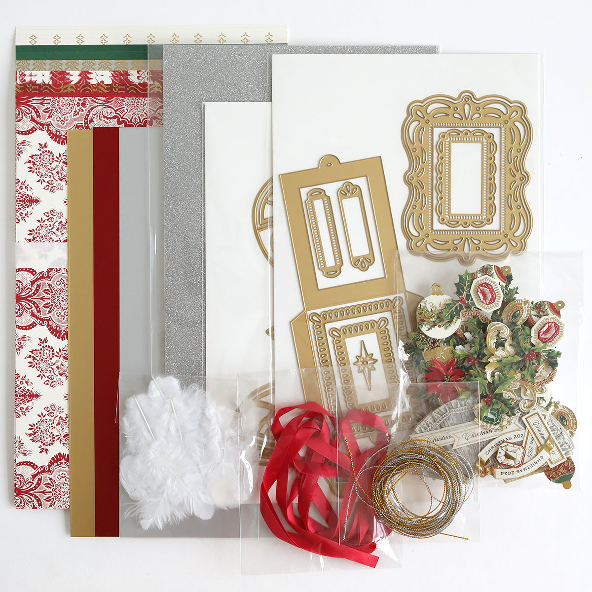 The Origami Ornaments Dies and Materials set is beautifully displayed on a flat surface, featuring patterned papers, cardstock, decorative cutouts, ribbons, white feathers, gold foil frames, 3D embellishments, and gold string.