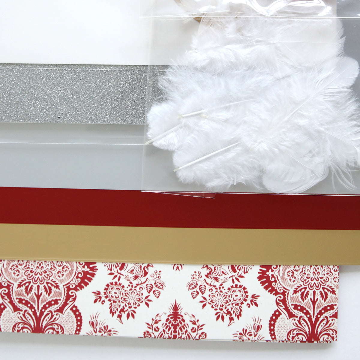 Discover the Origami Ornaments Dies and Materials, offering an array of crafting materials ideal for creating exquisite origami ornaments. The set includes white feathers, glittery silver paper, red and gold paper, and patterned paper with red designs—all ready to be transformed into stunning 3D embellishments.