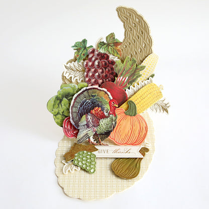 Show your gratitude with the Cornucopia Easel Card Dies—a set that lets you create an elegant pop-up card featuring a turkey, pumpkin, grapes, corn, and assorted vegetables, complete with the “Give thanks” sentiment on a cream-colored background. Perfect for card making or adding a festive touch to your Thanksgiving décor.