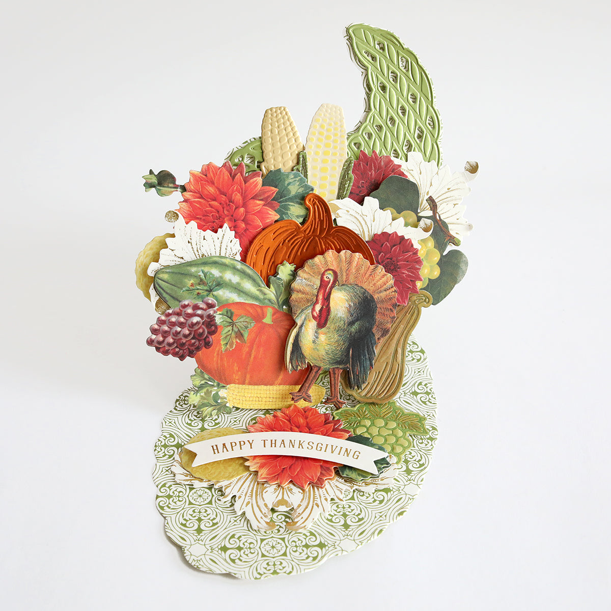 Celebrate Thanksgiving with a festive handmade card adorned with a turkey, pumpkins, corn, flowers, and a “Happy Thanksgiving” banner—all set against a crisp white background. Perfect for adding seasonal flair to your holiday décor or giving to loved ones, this charming design can be easily recreated using the Cornucopia Easel Card Dies for an extra-special touch. Ideal for card-making enthusiasts!.