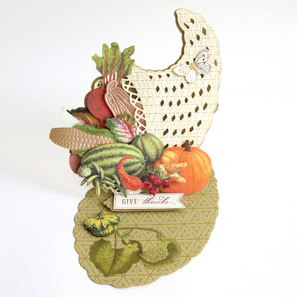 Create a stunning Thanksgiving card or festive table décor with the Cornucopia Easel Card Dies—featuring detailed vegetables, fruits, and a pumpkin on an intricately patterned base, complete with a “Give thanks” sign and butterfly accents on a cut-out background.