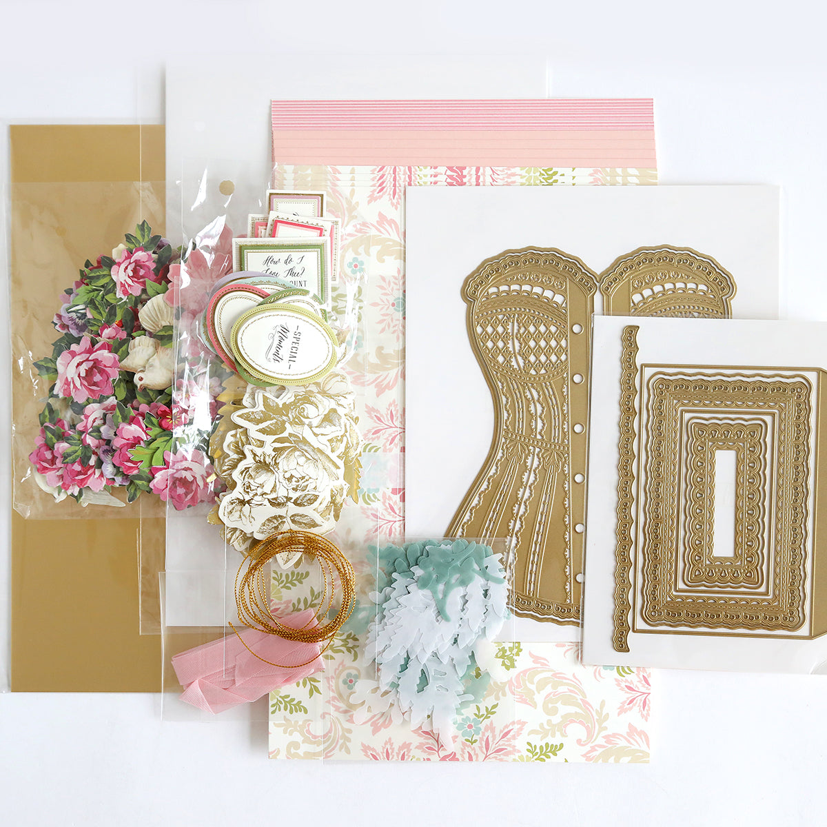 The Corset Album Dies and Materials set includes floral paper, decorative cutouts, ribbons, gold embossing templates, and intricate dies artfully arranged on a flat surface.