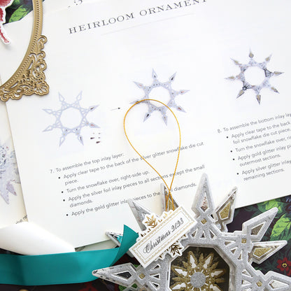 A Create 9 Class Instructions ornament, with color photos as Step by Step Instructions, is on a table next to a book. (Brand name: Anna Griffin)