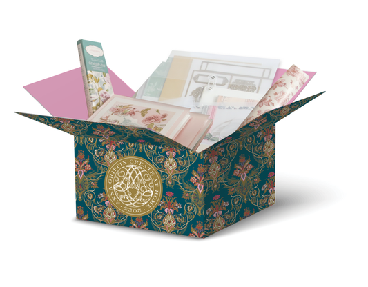 Anna Griffin | Create 2025: A floral-patterned box with a gold emblem, filled with assorted pastel stationery for papercrafting events—includes envelopes, cards, and decorative paper.