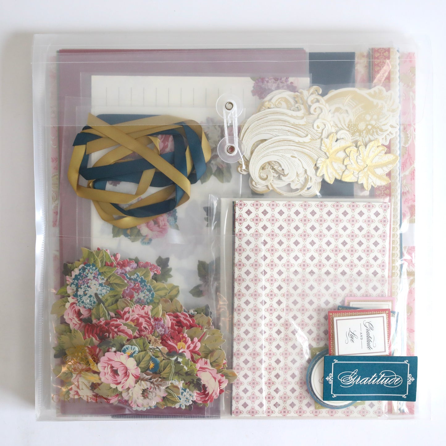 Anna Griffin | Create 2025: A clear folder filled with patterned papers, floral cutouts, decorative cards, ribbons, and ornate die-cuts—ideal for your next papercrafting event.