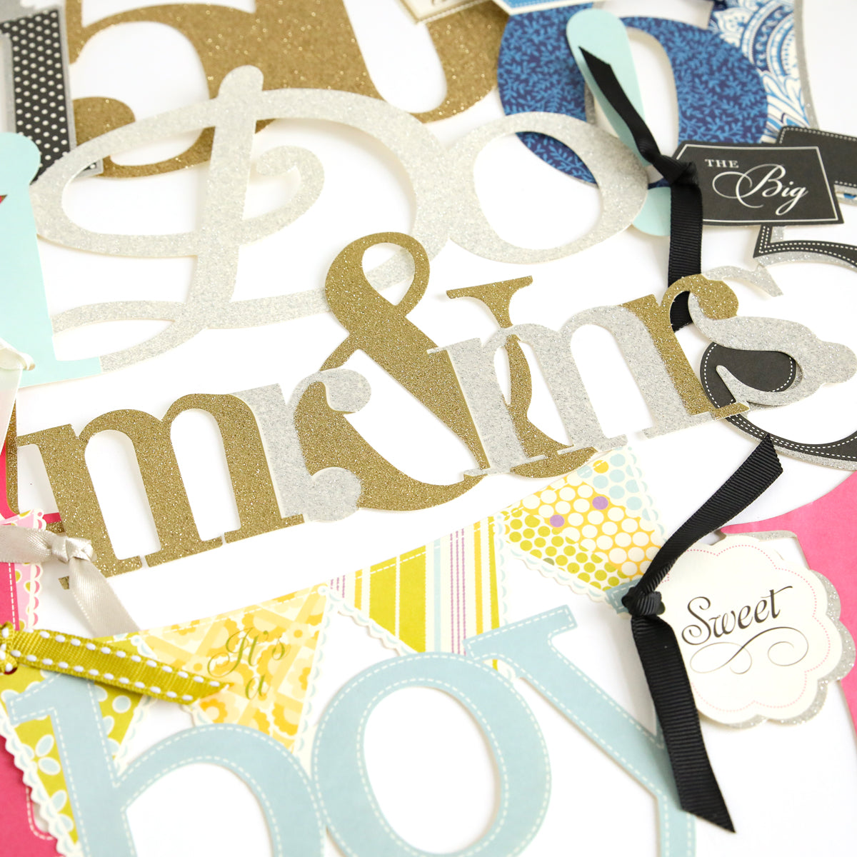 The Friends and Family Diecut Word Assortment features a variety of paper decorations, including glittery "mr & mrs" and "boy" cutouts, colorful pennants, oversized diecut numbers, and labeled tags on a white background—perfect for handmade cards or scrapbook pages.