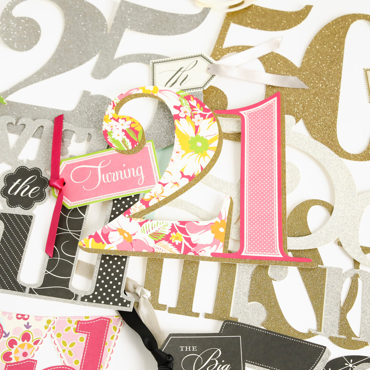 From the Friends and Family Diecut Word Assortment, a decorative cutout featuring "21" in pink and floral patterns and a coordinating "Turning" tag sits among glittery numeral accents—ideal for embellishing scrapbook layouts or handmade cards to mark a festive 21st birthday celebration.