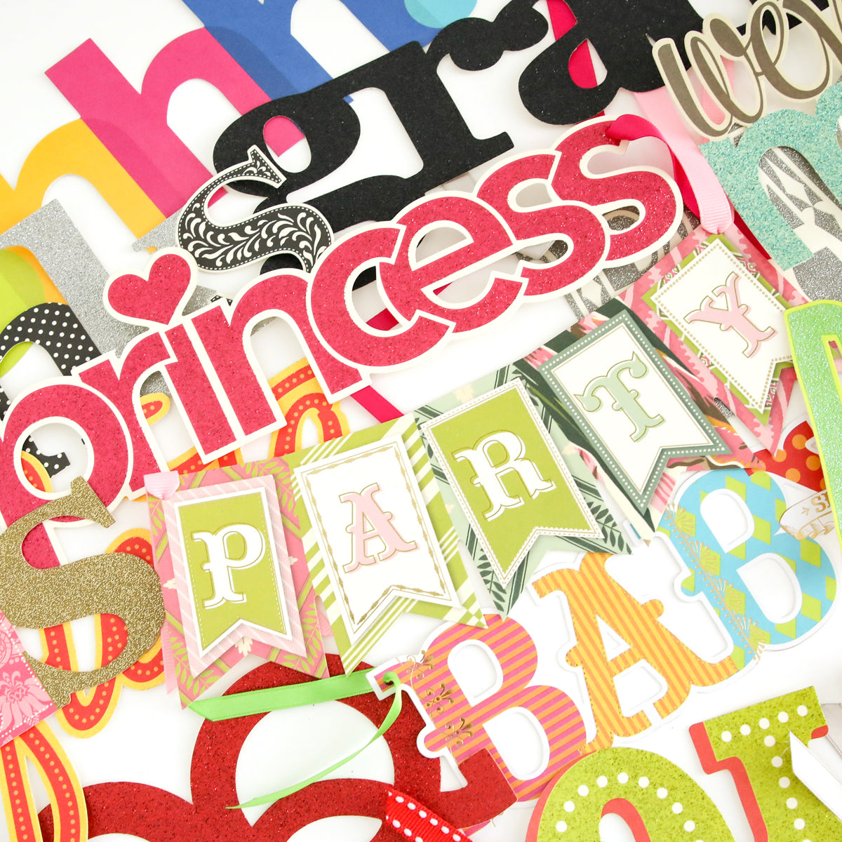 A scattered pile of vibrant diecut words from the Party Time Diecut Word Assortment—including phrases like "princess," "party," and "baby"—makes the perfect embellishment for scrapbook pages or handmade cards.