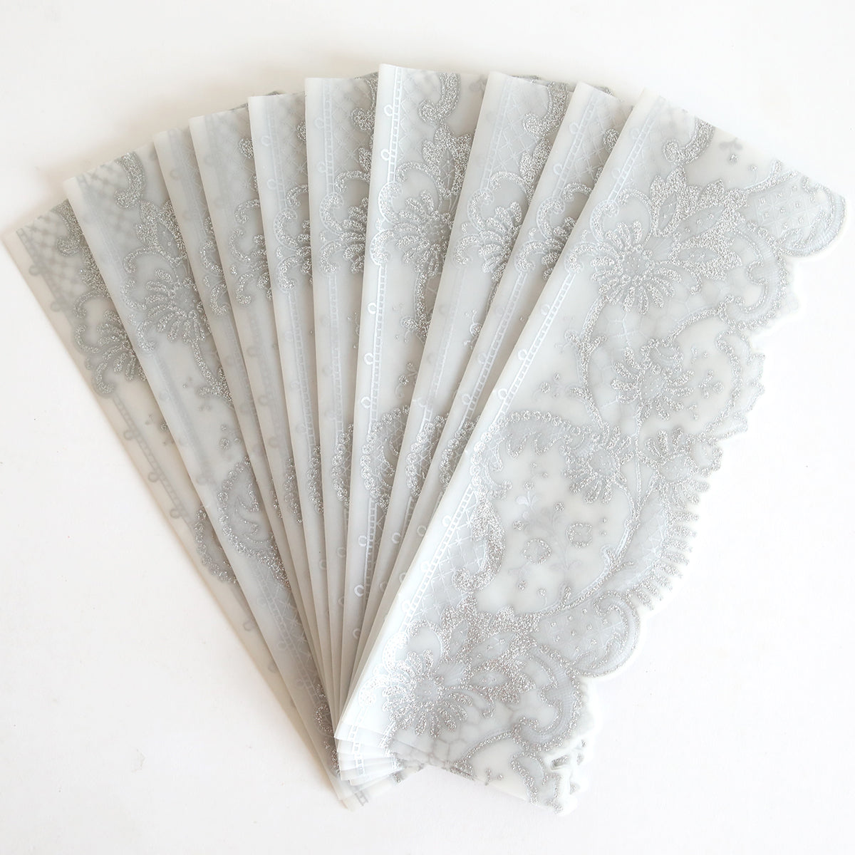 The Silver Lace Glitter Vellum Wrap 10 pack features translucent wraps with intricate silver lace glitter patterns, showcased beautifully against a white background.